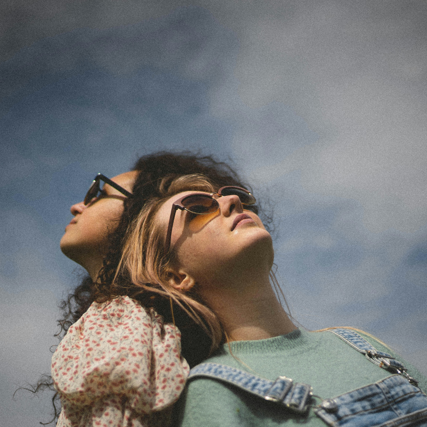 Två tjejer som står rygg mot rygg och en blå himmel med lätta slöjmoln