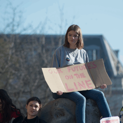 En tjej som sitter med ett plakat i famnen.