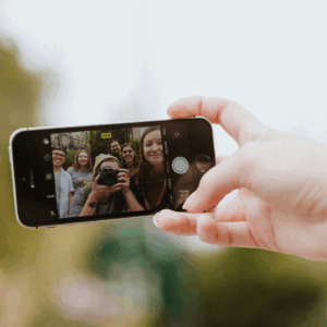 En hand som håller en mobiltelefon och tar kort på en grupp med unga